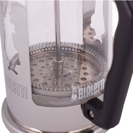 Nærbillede af Bialetti stempelkande med glasbeholder, metalfilter og sort håndtag i minimalistisk produktfoto.