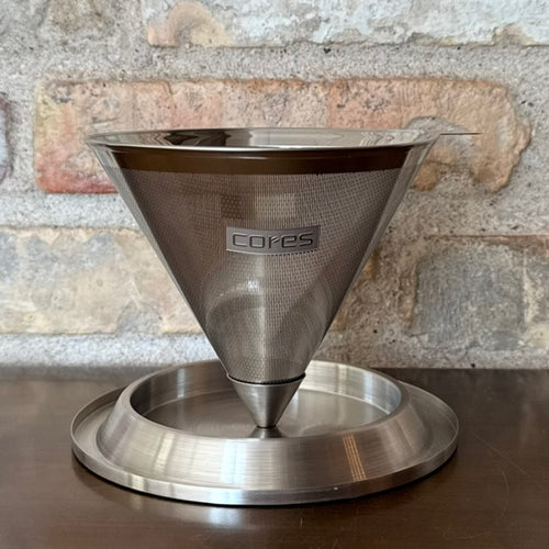 Permanent Cores kaffefilter i metal til pour-over, vist foran en murstensvæg.