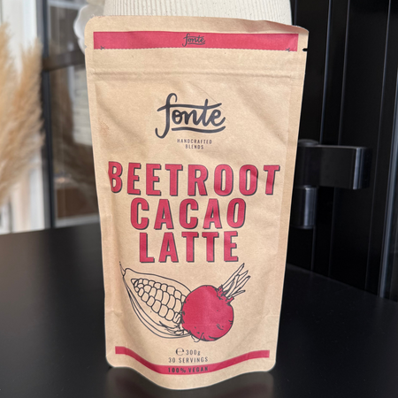 Pose med Fonte Beetroot Cacao Latte pulver i naturlig papirindpakning placeret i moderne café- og butiksmiljø.
