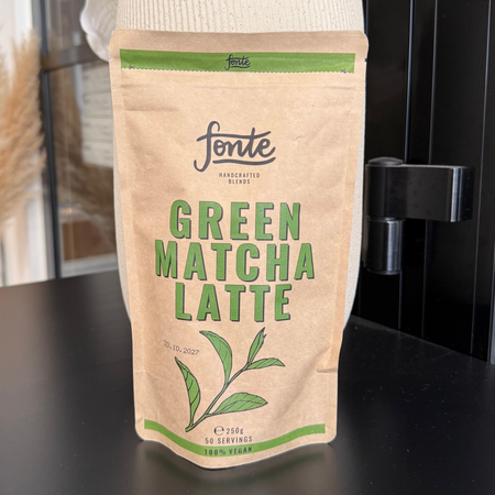Pose med Fonte Green Matcha Latte pulver i naturlig papirindpakning placeret i moderne café- og butiksmiljø.