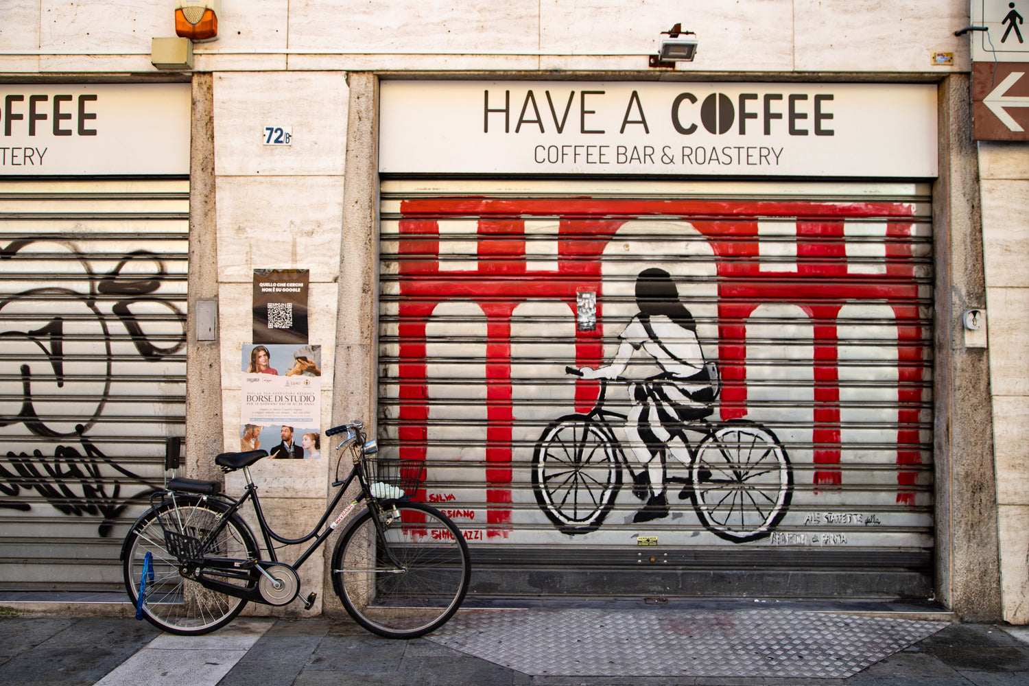 Facade til Have A Coffee Coffee Bar & Roastery med gadekunst på butiksskodde og parkeret cykel foran caféen i urbant bymiljø.