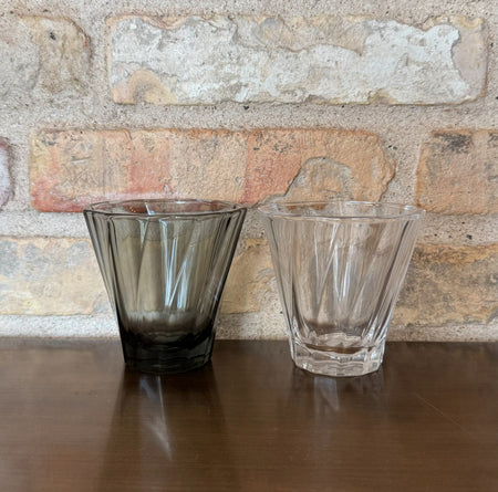 To gennemsigtige og mørke glas kaffekopper på en træhylde.