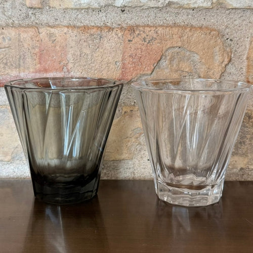 To gennemsigtige og mørke glas kaffekopper på en træhylde.